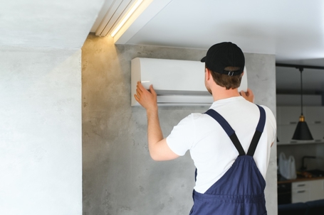 An HVAC technician wearing a uniform installs a ductless mini-split air conditioner in a modern home.