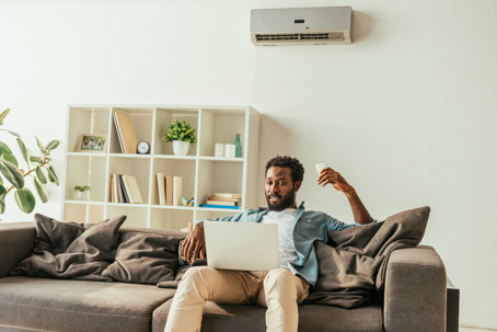A relaxed man works on a laptop while reclining on a comfortable sofa.