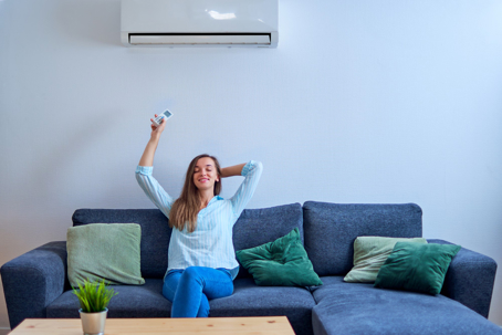 A woman smiles on her couch, holding a remote up at her new air conditioner.