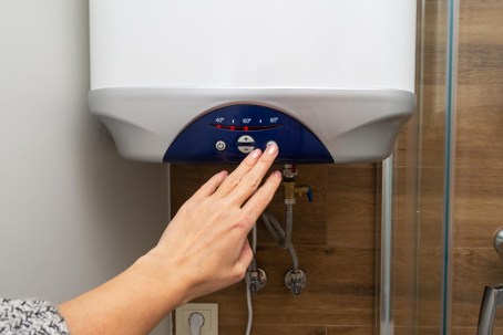 A hand adjusts the settings on a modern, wall-mounted water heater.