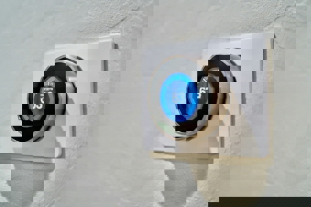 A smart thermostat mounted on a textured wall displays "HEAT SET TO 63."