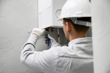 A technician wearing a hard hat works on a water heater.