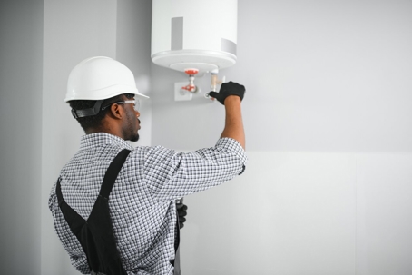 A technician in safety gear works on a white water heater.