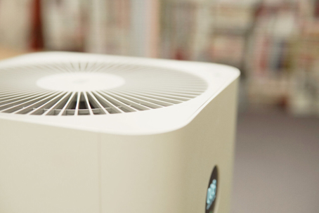 A close-up shows a white air purifier with circular grill, possibly indoors.