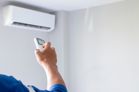 A person uses a remote to adjust a mini-split air conditioner mounted on a white wall.