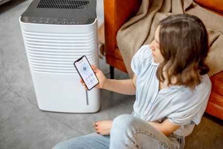 A woman sits next to a humidifier, holding a smartphone.
