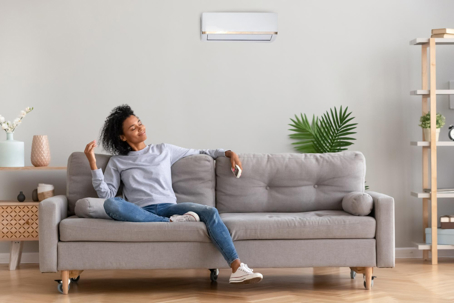 Woman relaxes on a sofa with an air conditioner overhead, enjoying a comfortable room.