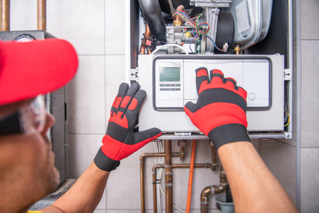 A technician in a red cap and gloves services a home boiler