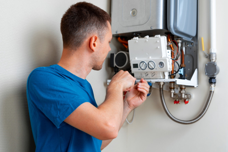 A technician in a blue shirt repairs a wall-mounted water heater.